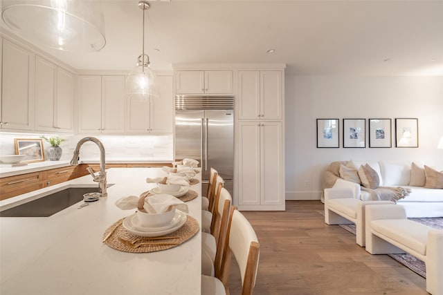 kitchen with sink, light hardwood / wood-style flooring, white cabinetry, hanging light fixtures, and stainless steel built in refrigerator