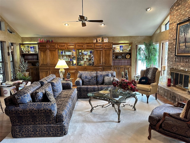 living room featuring lofted ceiling, a brick fireplace, ceiling fan, and light wood-type flooring