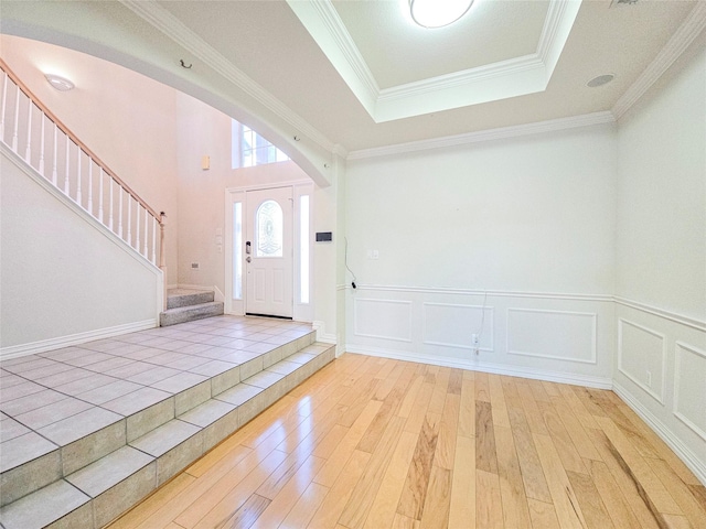 foyer entrance with a tray ceiling, crown molding, and light hardwood / wood-style floors