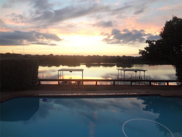 pool at dusk with a water view and a pergola