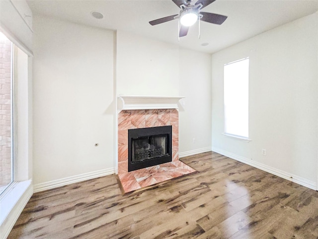 unfurnished living room with a tiled fireplace, hardwood / wood-style floors, and ceiling fan