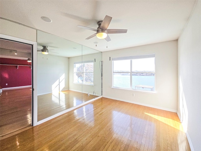 empty room featuring a water view, ceiling fan, and light hardwood / wood-style floors