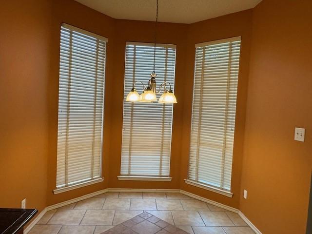 unfurnished dining area with baseboards, tile patterned flooring, and an inviting chandelier