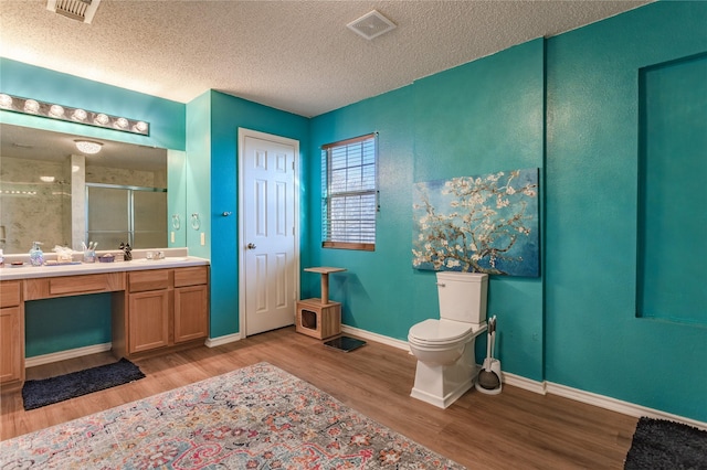 bathroom featuring wood-type flooring, toilet, a shower with door, and a textured ceiling