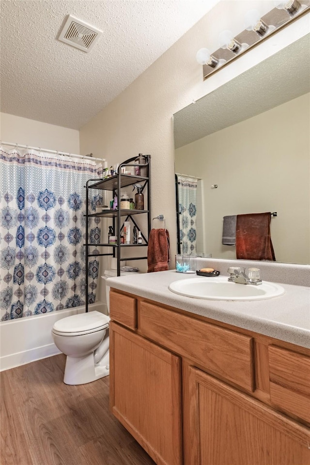 full bathroom with wood-type flooring, vanity, shower / tub combo, toilet, and a textured ceiling