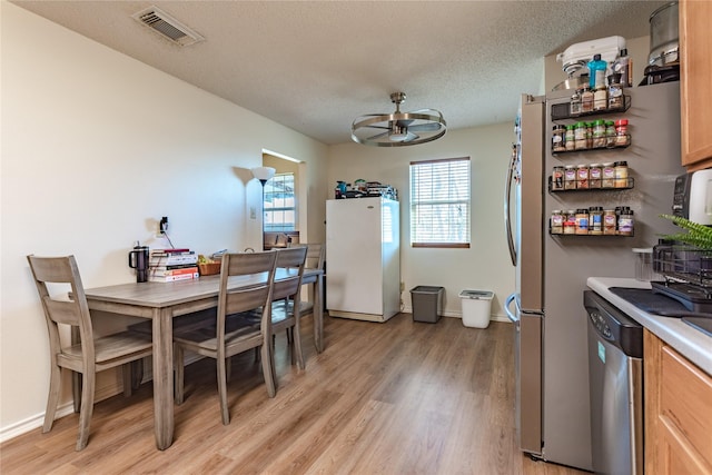 dining space with ceiling fan, a textured ceiling, and light wood-type flooring