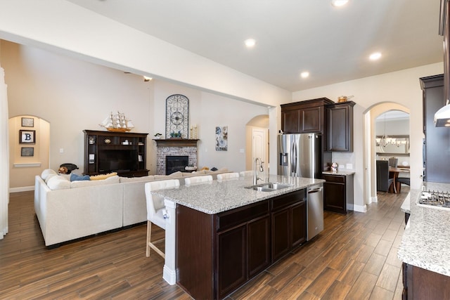 kitchen with appliances with stainless steel finishes, an island with sink, sink, light stone counters, and a brick fireplace