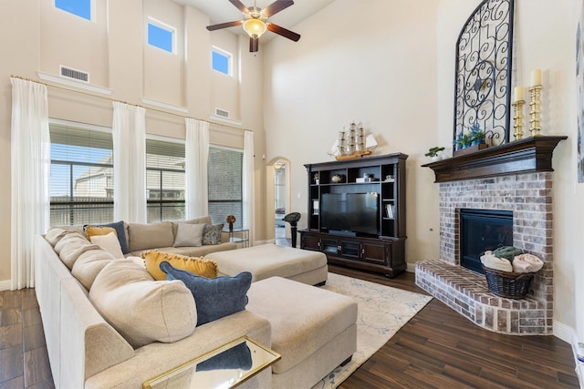 living room featuring ceiling fan, a fireplace, dark hardwood / wood-style floors, and a high ceiling