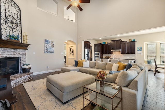 living room with a towering ceiling, sink, hardwood / wood-style flooring, ceiling fan, and a brick fireplace