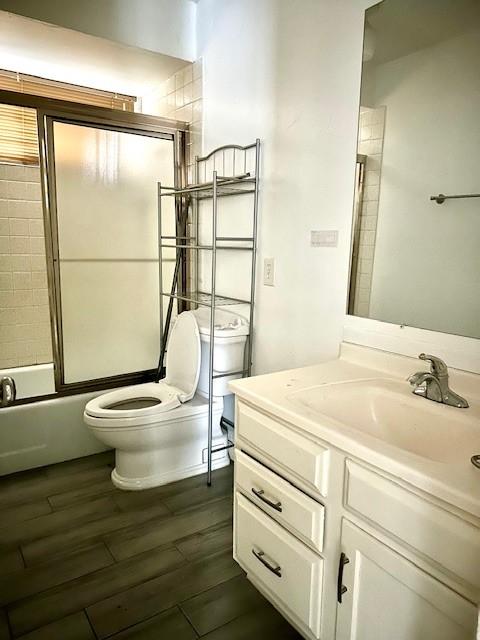 full bathroom featuring hardwood / wood-style flooring, vanity, shower / bath combination with glass door, and toilet