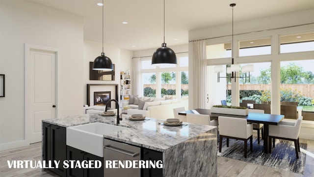 kitchen featuring light hardwood / wood-style floors, decorative light fixtures, light stone countertops, and a kitchen island with sink