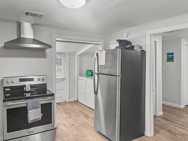 kitchen featuring wall chimney range hood, a textured ceiling, stainless steel appliances, and washing machine and clothes dryer