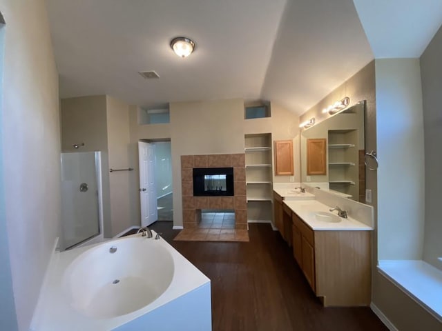 bathroom featuring lofted ceiling, hardwood / wood-style flooring, a tile fireplace, vanity, and independent shower and bath