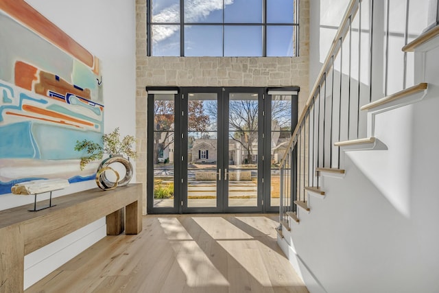 foyer entrance featuring a towering ceiling, light wood-type flooring, and french doors