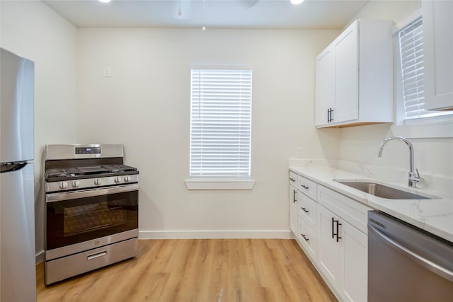 kitchen with white cabinetry, sink, stainless steel appliances, light stone countertops, and light wood-type flooring