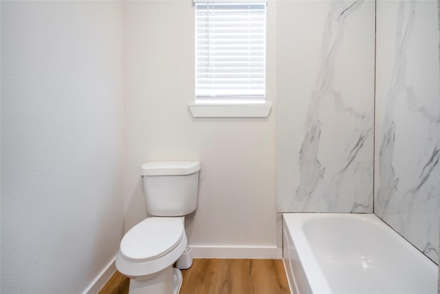 bathroom with hardwood / wood-style flooring, toilet, and a tub to relax in