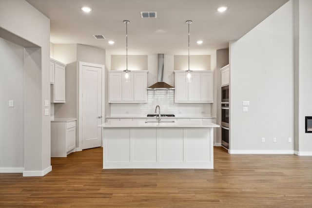 kitchen featuring white cabinetry, decorative light fixtures, an island with sink, decorative backsplash, and wall chimney range hood