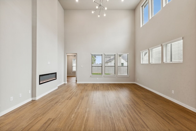 unfurnished living room with a notable chandelier, a towering ceiling, and light hardwood / wood-style flooring