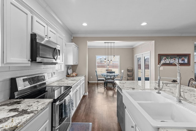 kitchen featuring sink, appliances with stainless steel finishes, white cabinetry, hanging light fixtures, and decorative backsplash