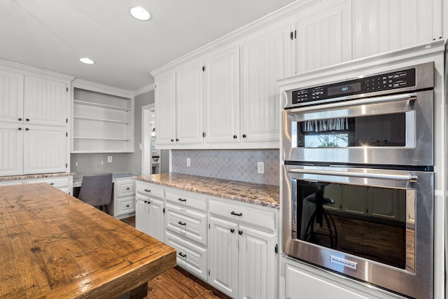 kitchen featuring double oven, built in desk, ornamental molding, and white cabinets