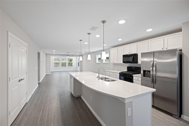 kitchen featuring sink, a kitchen island with sink, black appliances, white cabinets, and decorative light fixtures