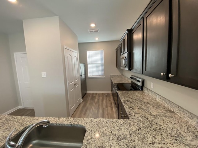 kitchen featuring sink, stainless steel appliances, light stone counters, dark brown cabinetry, and wood-type flooring