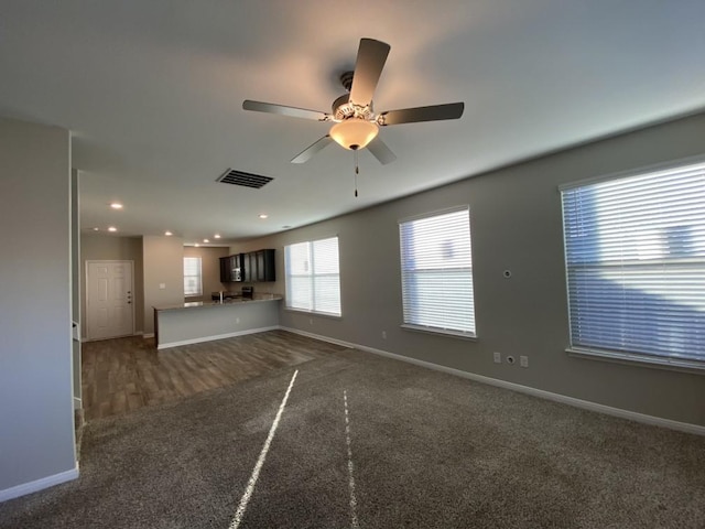 unfurnished living room with ceiling fan and dark colored carpet