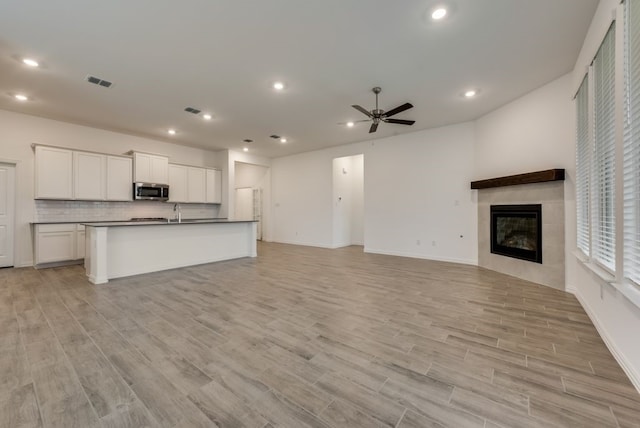 unfurnished living room with a tiled fireplace, sink, light hardwood / wood-style floors, and ceiling fan