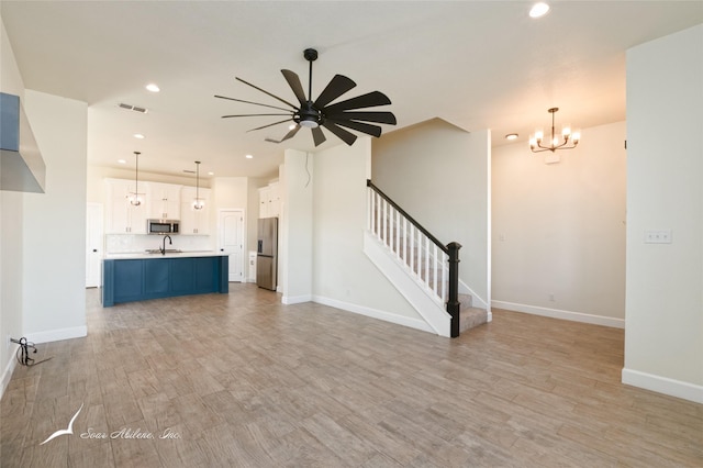 unfurnished living room with sink, ceiling fan with notable chandelier, and light hardwood / wood-style floors