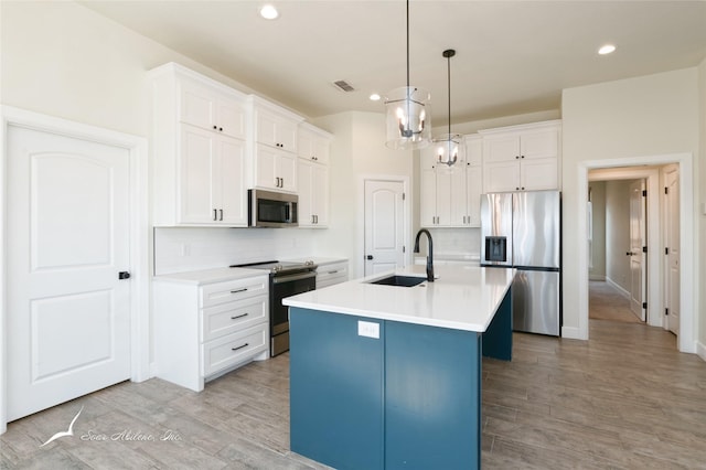 kitchen with sink, appliances with stainless steel finishes, white cabinetry, a center island with sink, and decorative light fixtures