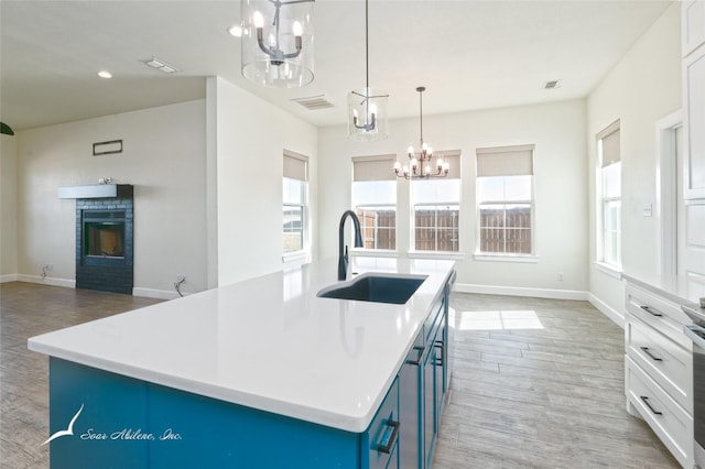 kitchen with sink, a kitchen island with sink, light hardwood / wood-style floors, blue cabinets, and decorative light fixtures