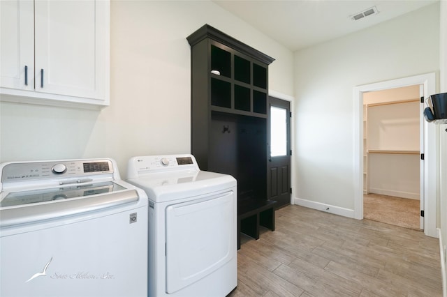 clothes washing area with cabinets, washer and clothes dryer, and light hardwood / wood-style flooring