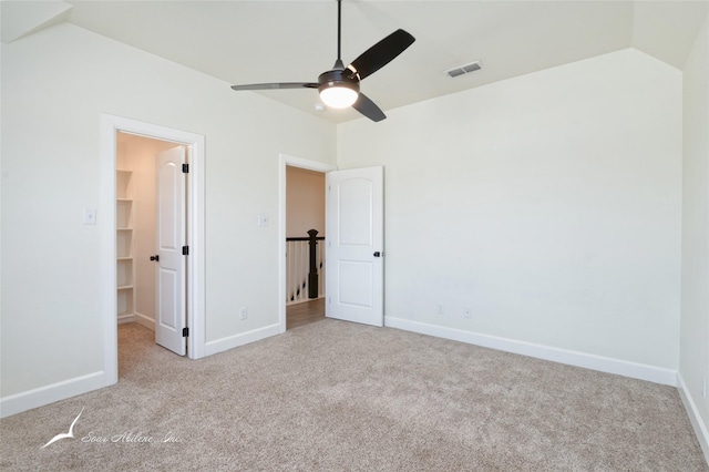 unfurnished bedroom with lofted ceiling, a walk in closet, light colored carpet, a closet, and ceiling fan