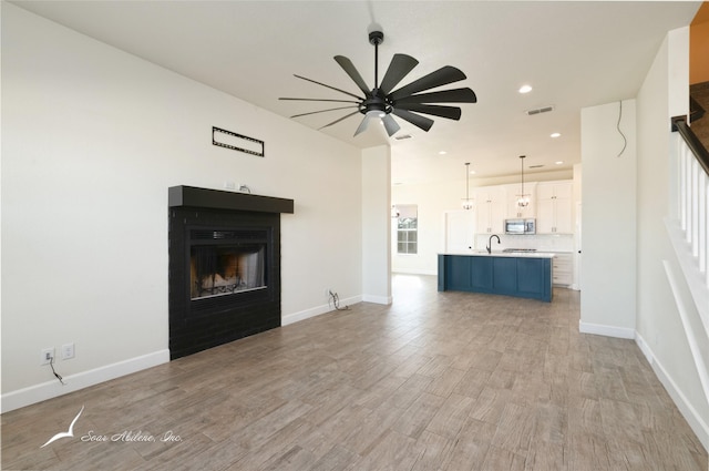 unfurnished living room featuring ceiling fan, light hardwood / wood-style floors, and sink