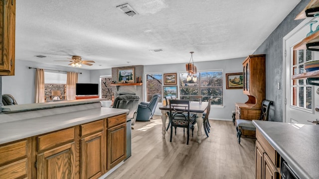 kitchen featuring ceiling fan, a fireplace, a textured ceiling, decorative light fixtures, and light wood-type flooring