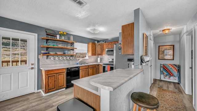 kitchen with stainless steel appliances, a kitchen breakfast bar, a healthy amount of sunlight, a textured ceiling, and kitchen peninsula