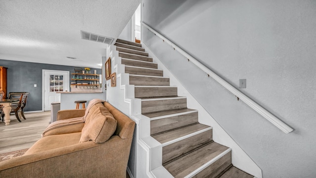 staircase with hardwood / wood-style floors, a textured ceiling, and indoor bar