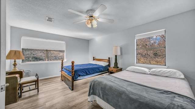 bedroom with multiple windows, a textured ceiling, ceiling fan, and light hardwood / wood-style flooring