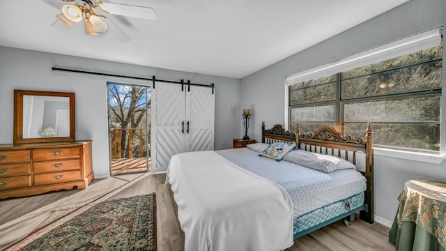 bedroom with multiple windows, a barn door, ceiling fan, and light wood-type flooring