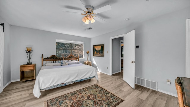 bedroom with a barn door, ceiling fan, and light hardwood / wood-style flooring