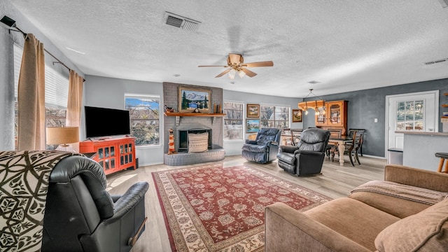 living room featuring a healthy amount of sunlight, a brick fireplace, light wood-type flooring, and a textured ceiling