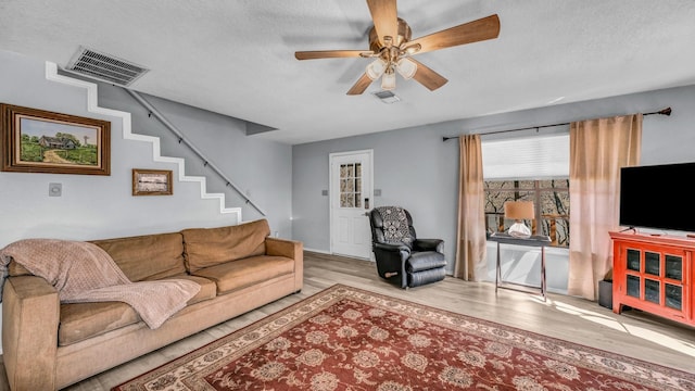 living room with ceiling fan, a textured ceiling, and light wood-type flooring