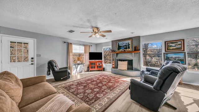 living room featuring ceiling fan, light hardwood / wood-style floors, a brick fireplace, and a textured ceiling