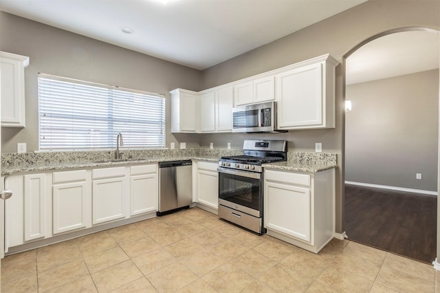 kitchen with appliances with stainless steel finishes, white cabinetry, sink, light tile patterned floors, and light stone counters