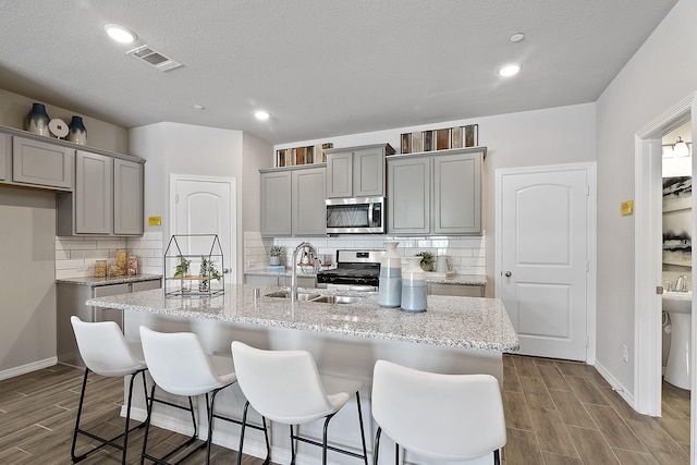 kitchen featuring sink, gray cabinets, stainless steel appliances, and a center island with sink