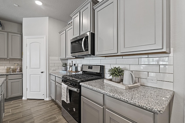 kitchen with light stone counters, gray cabinetry, appliances with stainless steel finishes, and backsplash