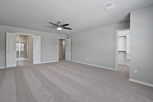 unfurnished bedroom featuring ensuite bath, ceiling fan, light carpet, a spacious closet, and a closet