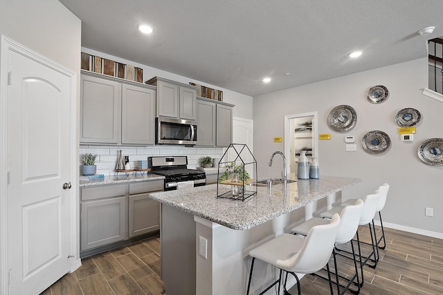 kitchen with gray cabinets, appliances with stainless steel finishes, sink, and a center island with sink