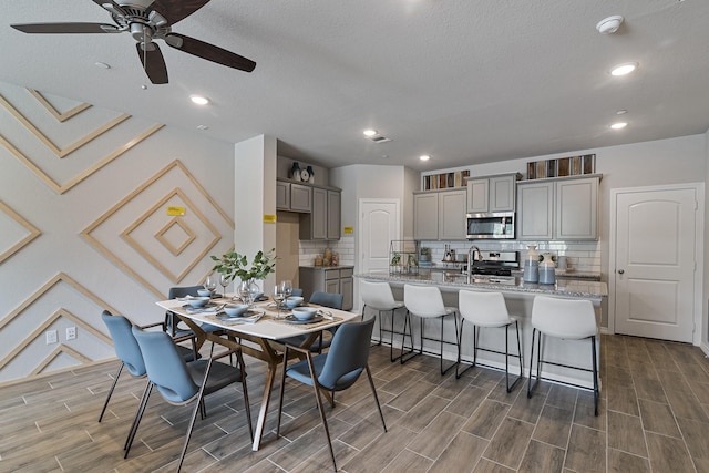 kitchen featuring sink, gray cabinetry, stainless steel appliances, light stone counters, and a kitchen bar