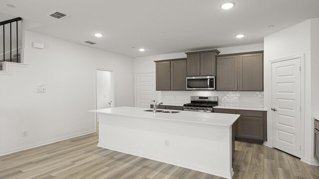 kitchen featuring a sink, light countertops, light wood-style floors, stainless steel appliances, and an island with sink